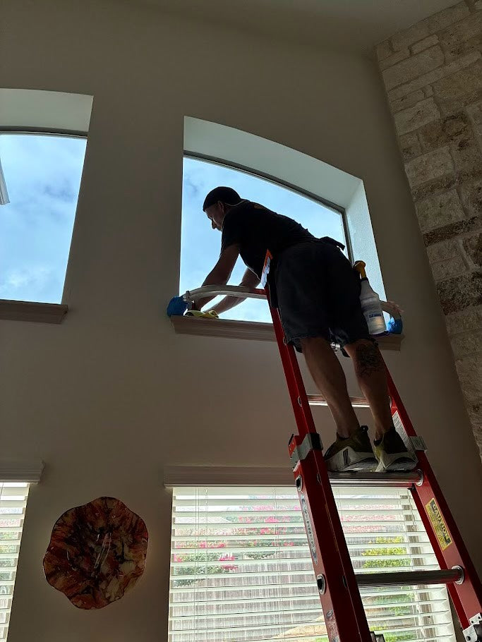 Person on a ladder applying window tint in a room with natural light